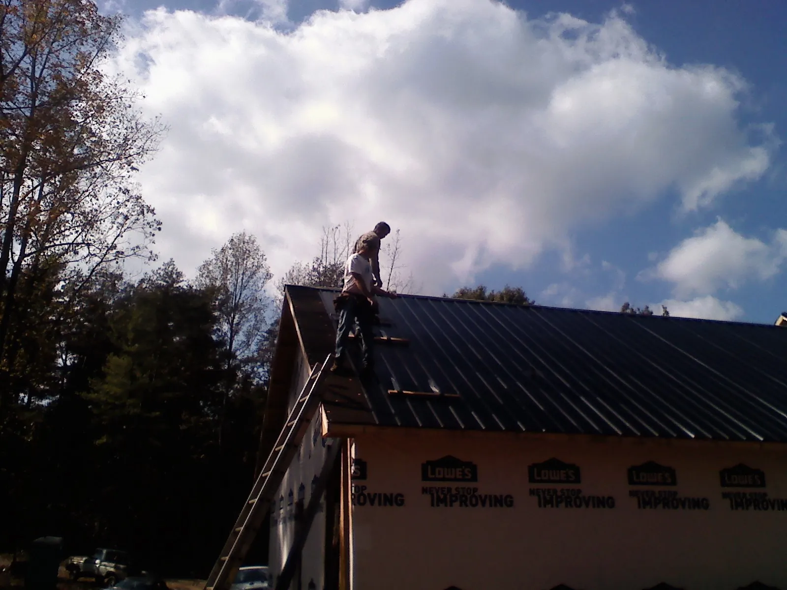 Roofer fastening dark metal panels high against a cloudy sky, from a Roof Inspection job in Des Plaines