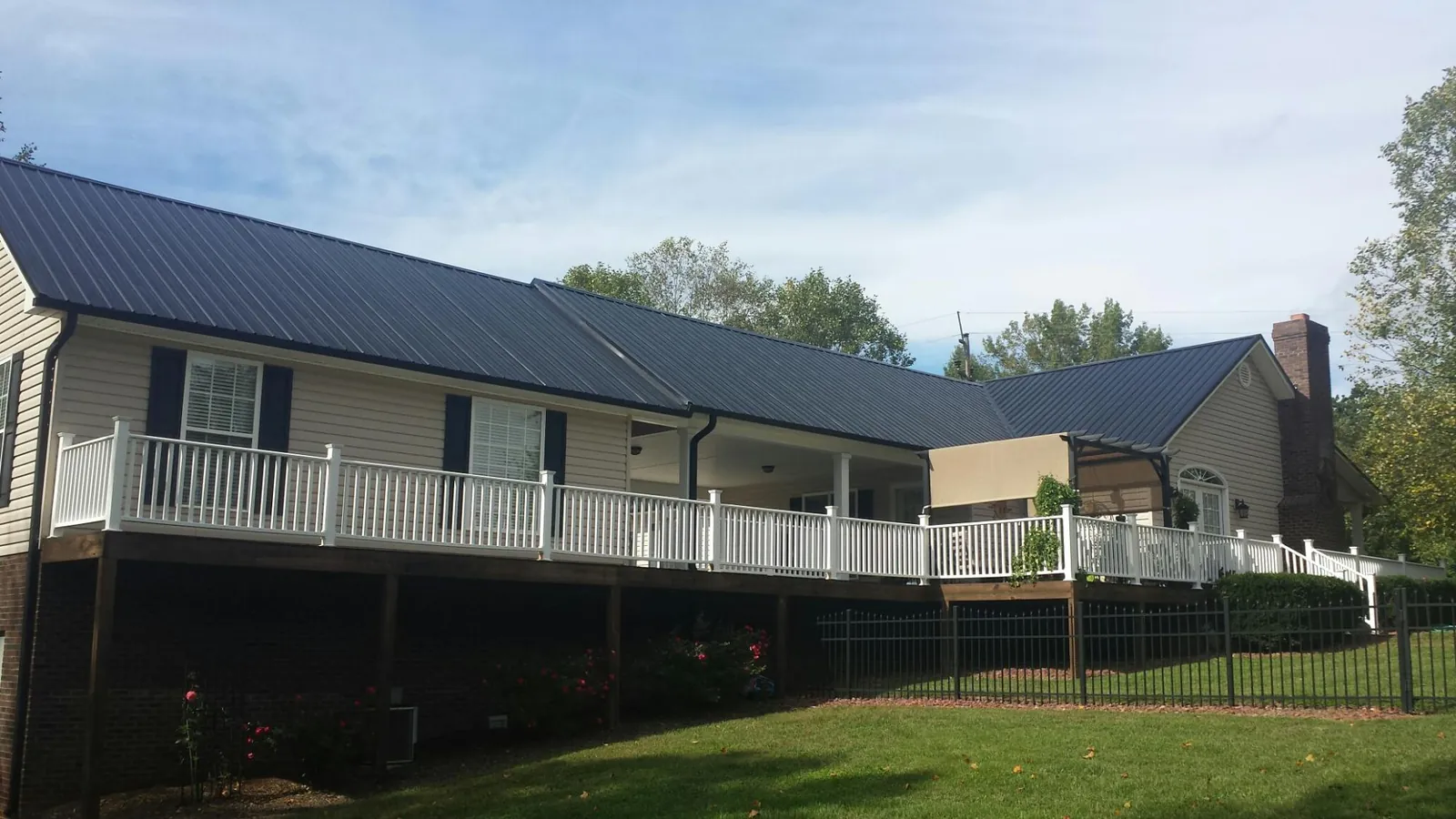Black metal roof above a long white railed deck on a hillside home in Des Plaines