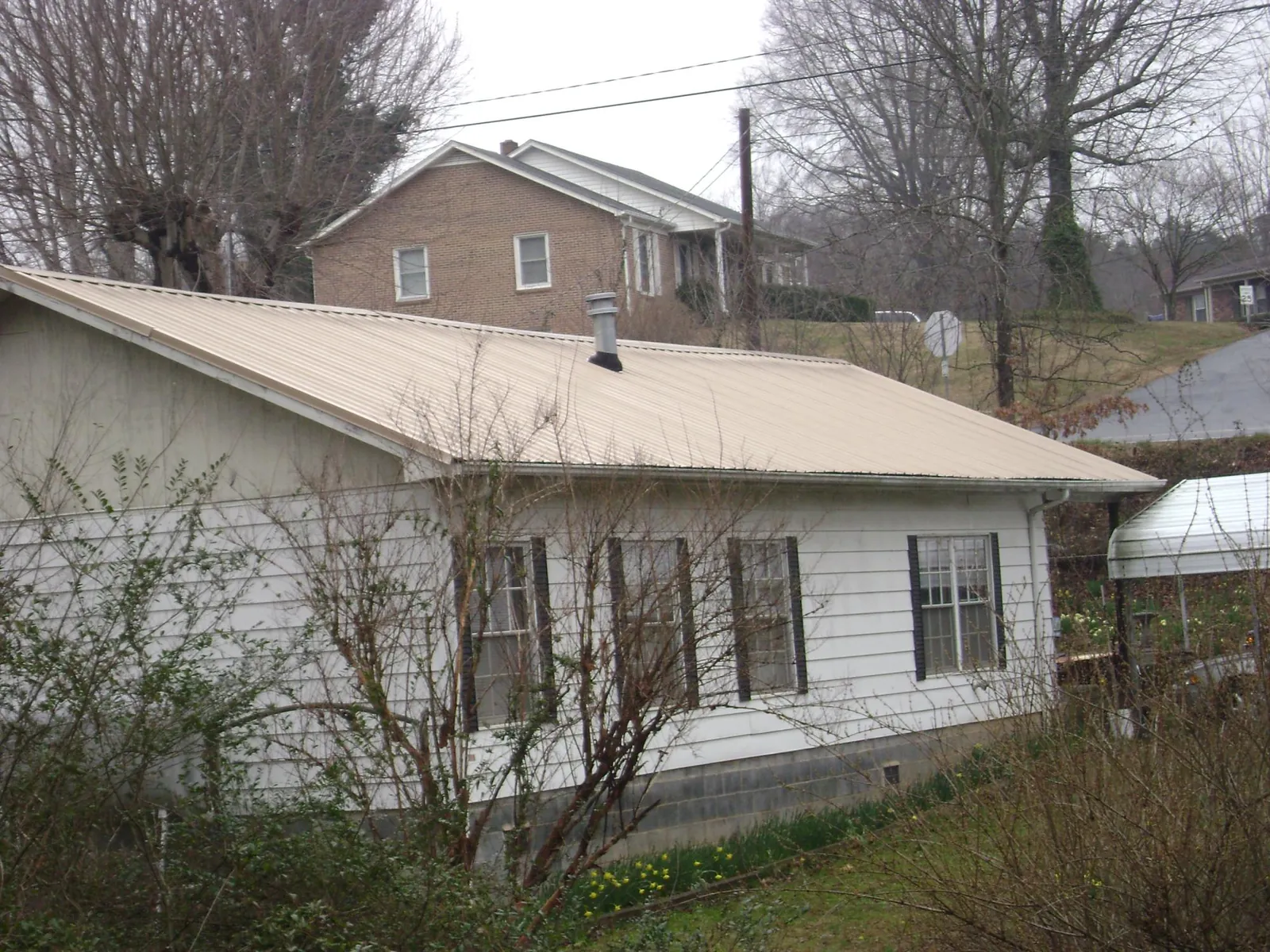 Tan metal roof on a white sided house set into a hillside — Commercial Roofing by Roofing Brothers in Des Plaines